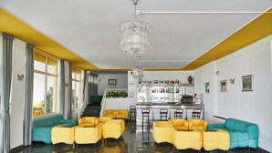 Amplia habitación con sofás amarillos y turquesas, una zona de bar con taburetes y una escalera que lleva a un nivel superior.