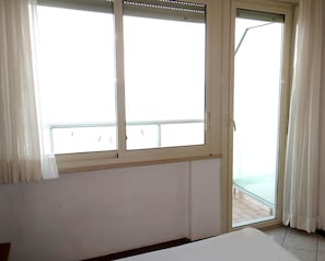 Una habitación con un ventanal grande, una puerta corrediza de vidrio y una cama.