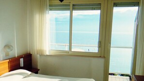 Un dormitorio con cama, mesita de noche, ventana con vista al mar y balcón.