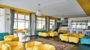Un hall de hotel con asientos amarillos y aguamarina, una zona de bar y ventanas amplias.