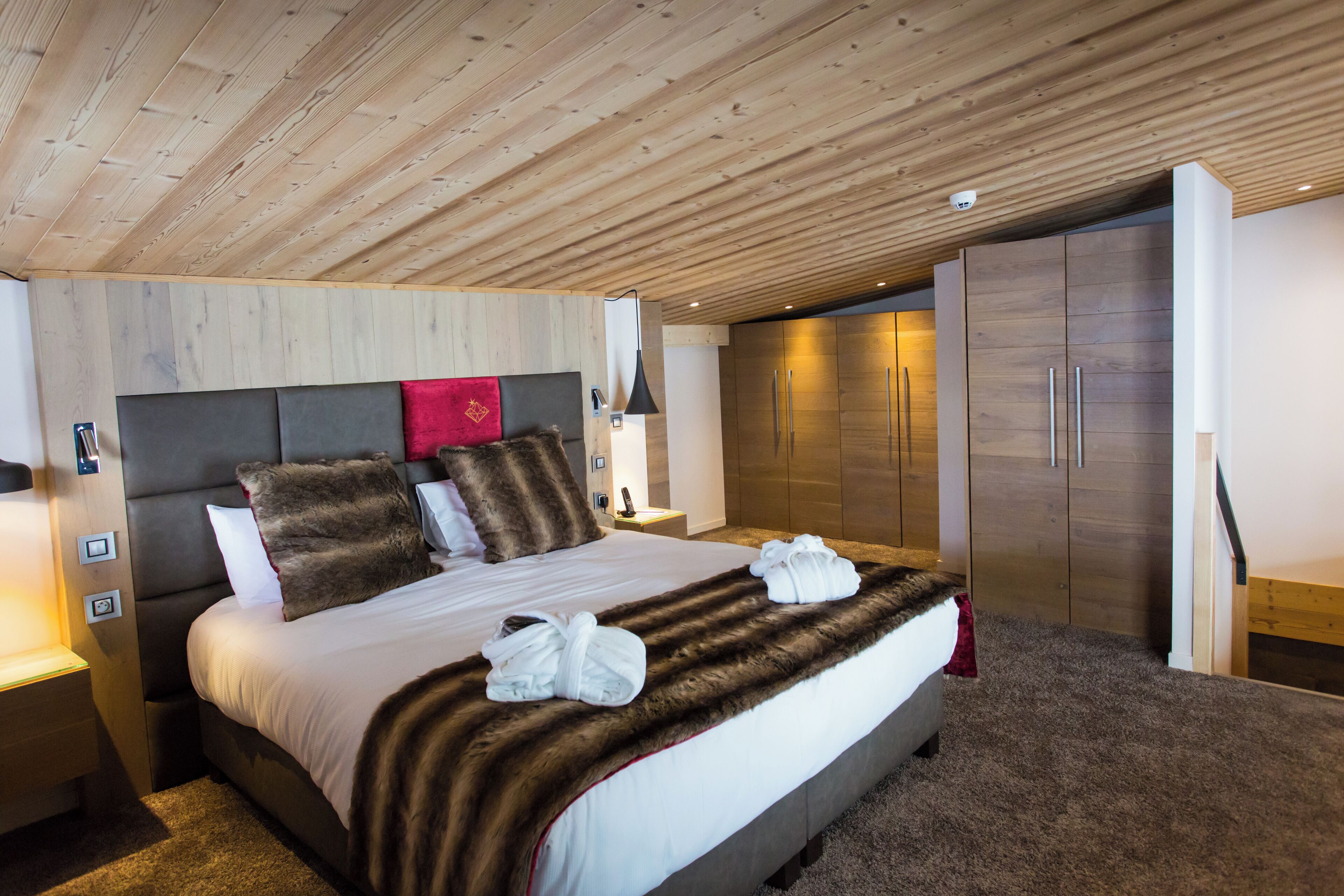 A modern hotel room with a large bed, wooden ceiling, and a wardrobe.
