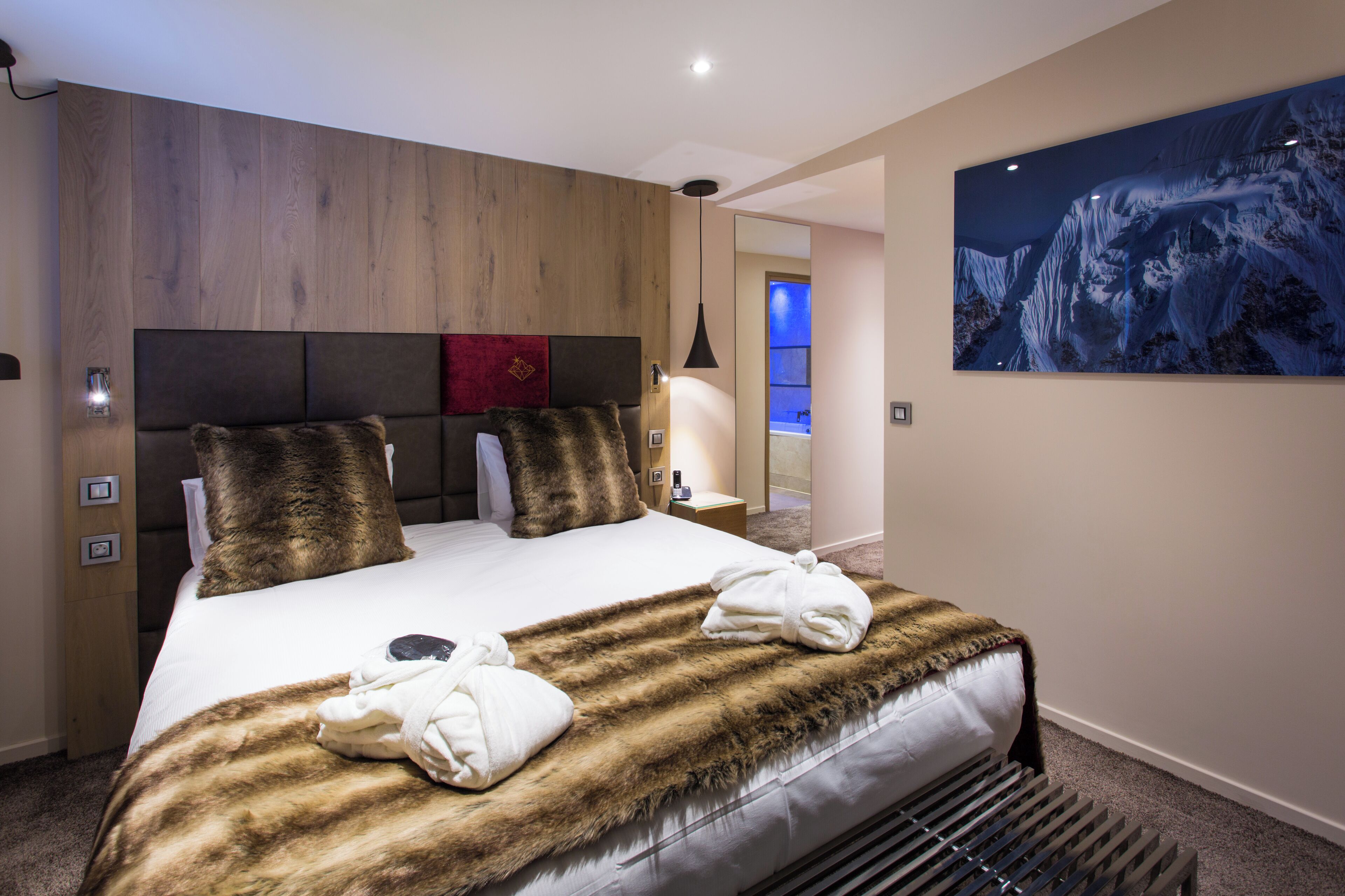 A hotel room with a large bed, wooden paneling on the walls, a mounted artwork, and a nightstand with a lamp.