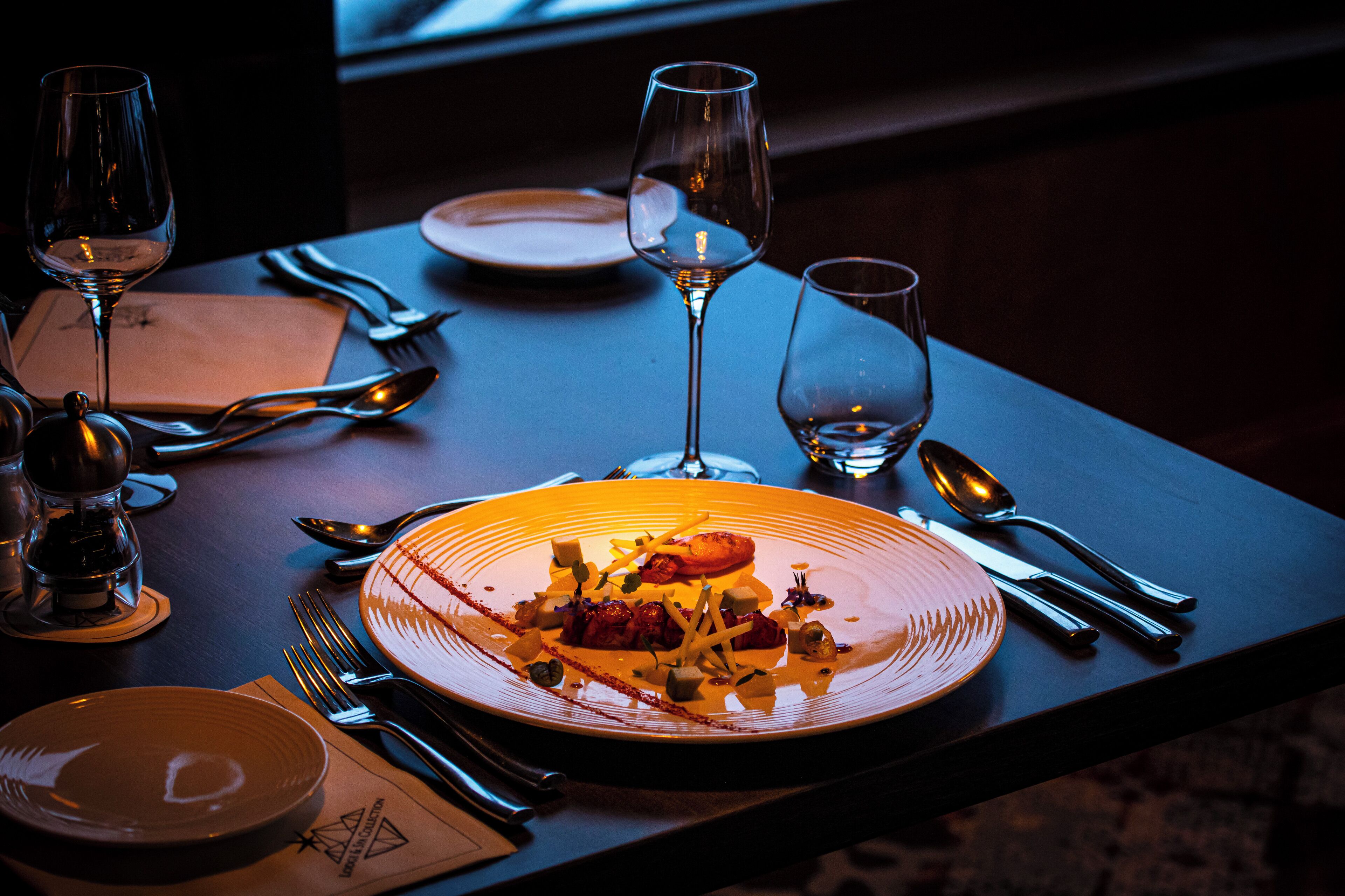A dining table set with plates, cutlery, and glasses, with a plate of food in the center.