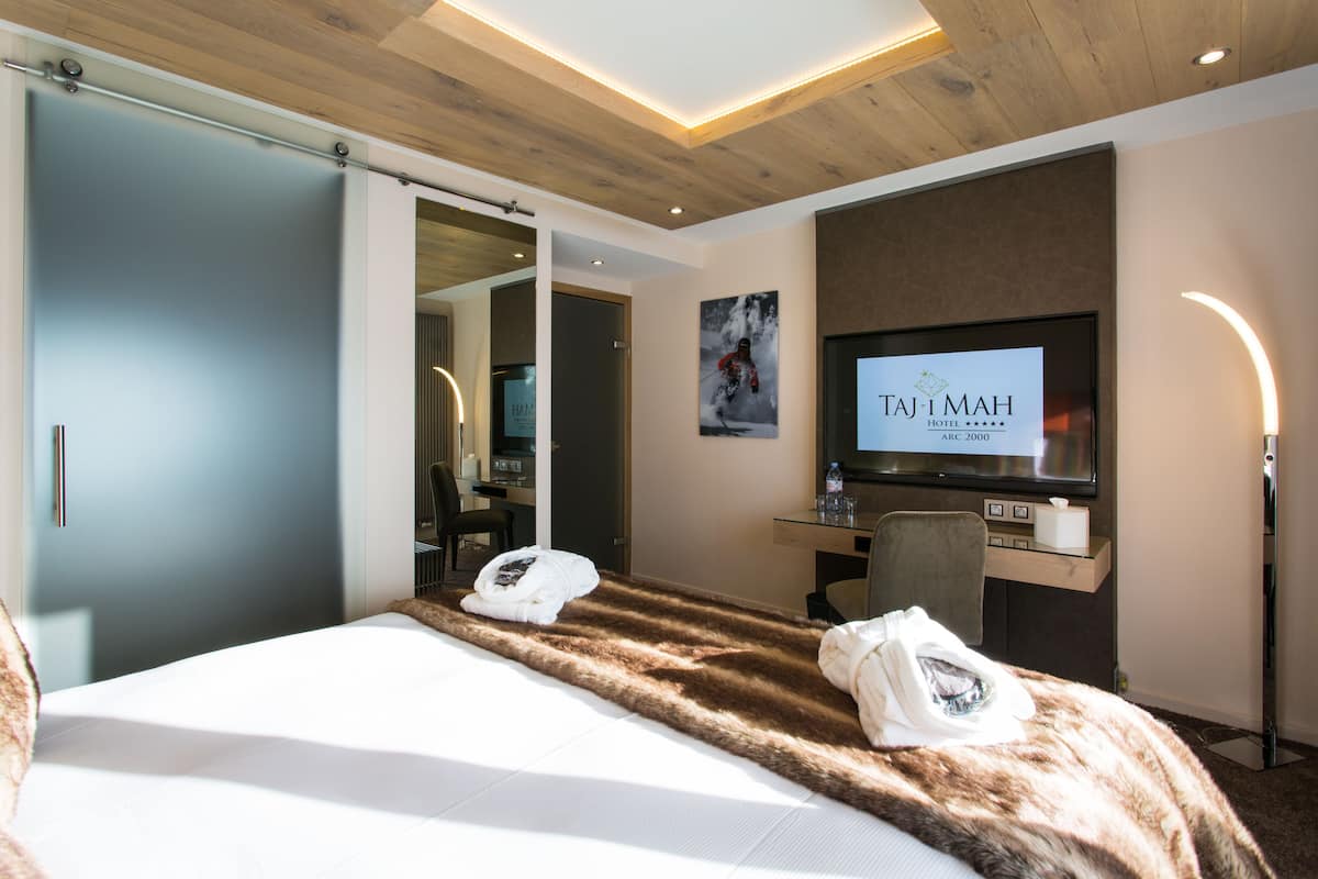 Moderni hotellihuone, jossa on suuri sänky, työpöytä tietokoneella, taulutelevisio ja peili.