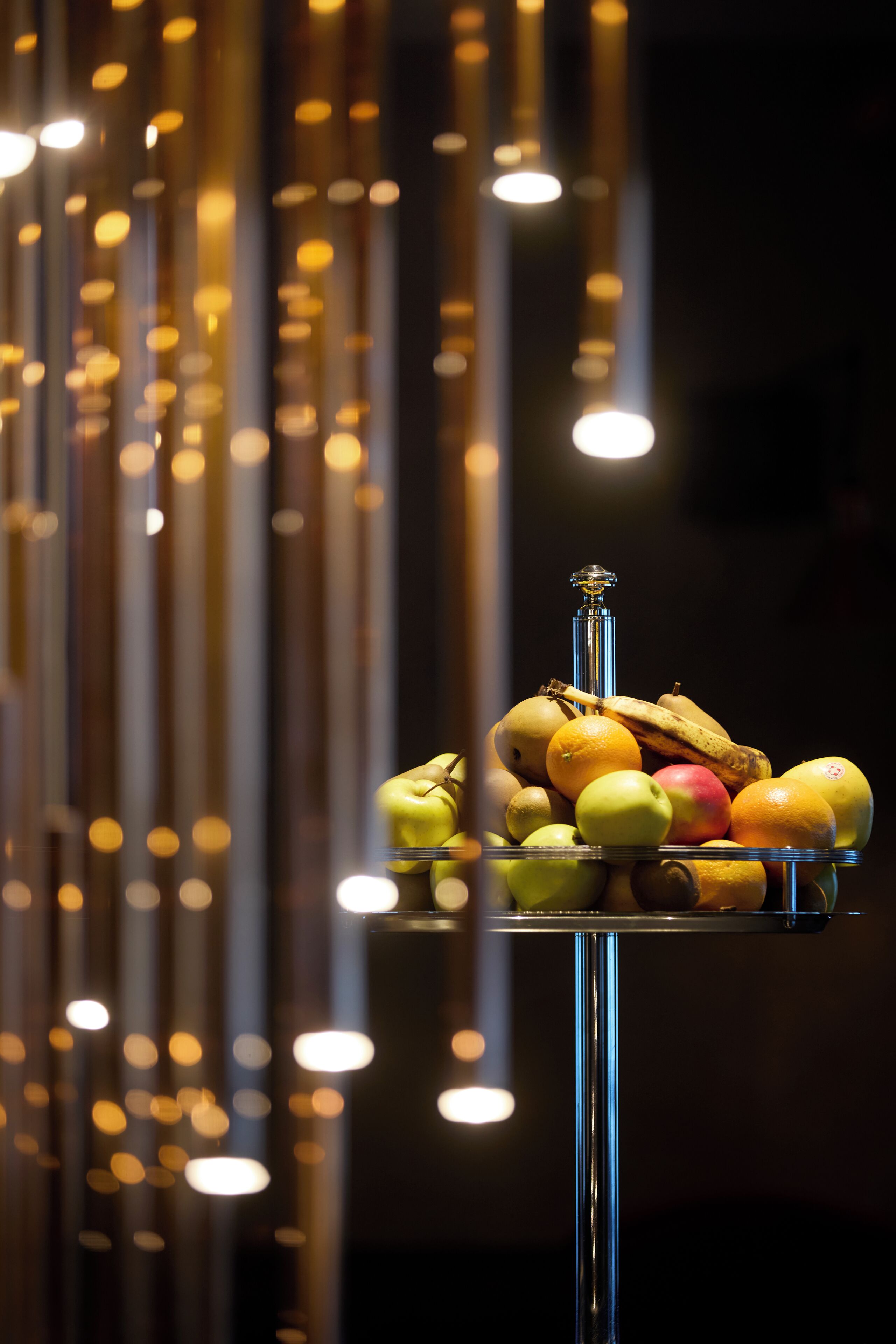 Fruitpresentatie op een reflecterend plateau met donkere achtergrond en hangende verlichting.