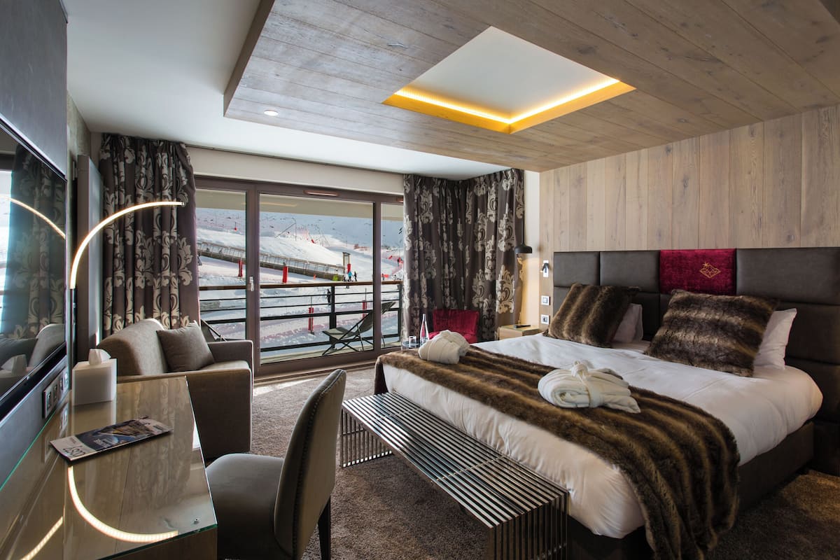 Moderni hotellihuone, jossa on suuri sänky, työpöytä ja tuoli. Ikkunoista avautuu näkymä lumiseen maisemaan.