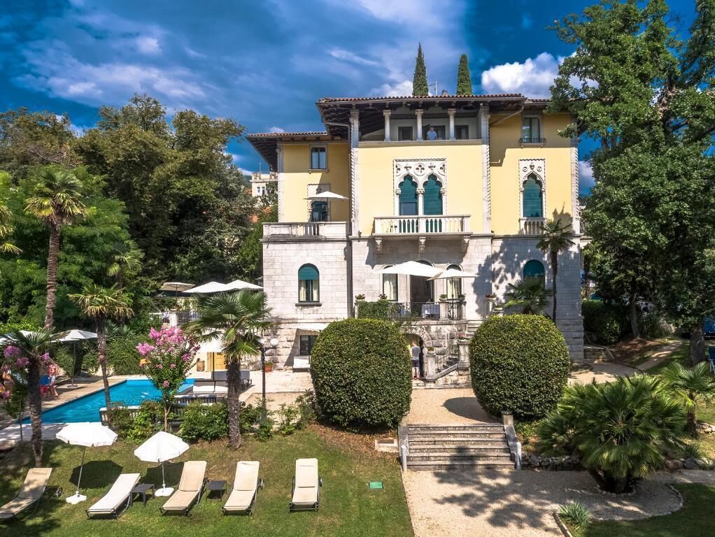 Un edificio grande con piscina, múltiples sillas de descanso y jardines bien cuidados.