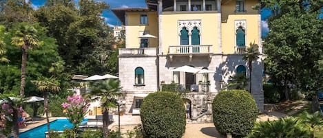 Un edificio grande con piscina, múltiples sillas de descanso y jardines bien cuidados.