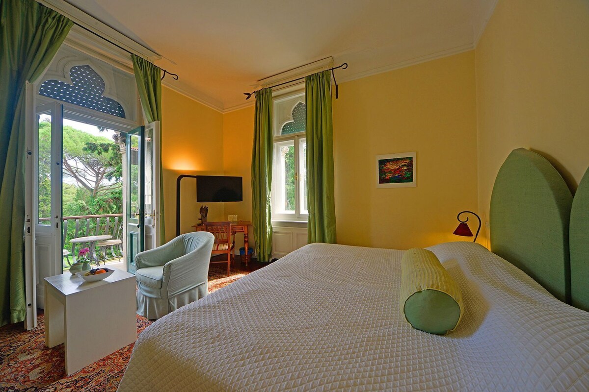 Un dormitorio con cama, una silla, un escritorio, un televisor y una ventana con cortinas.