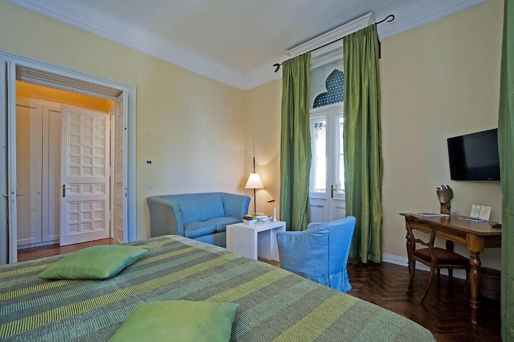 Habitación de hotel con cama, escritorio, silla, televisor y ventana con cortinas.