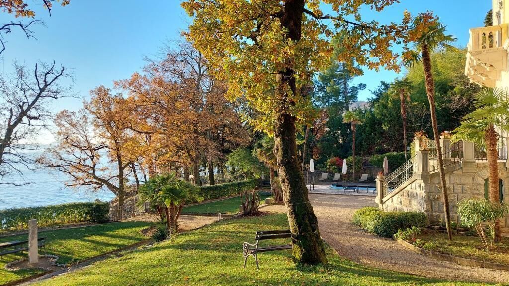 A park with a pathway, benches, and a building with a staircase.