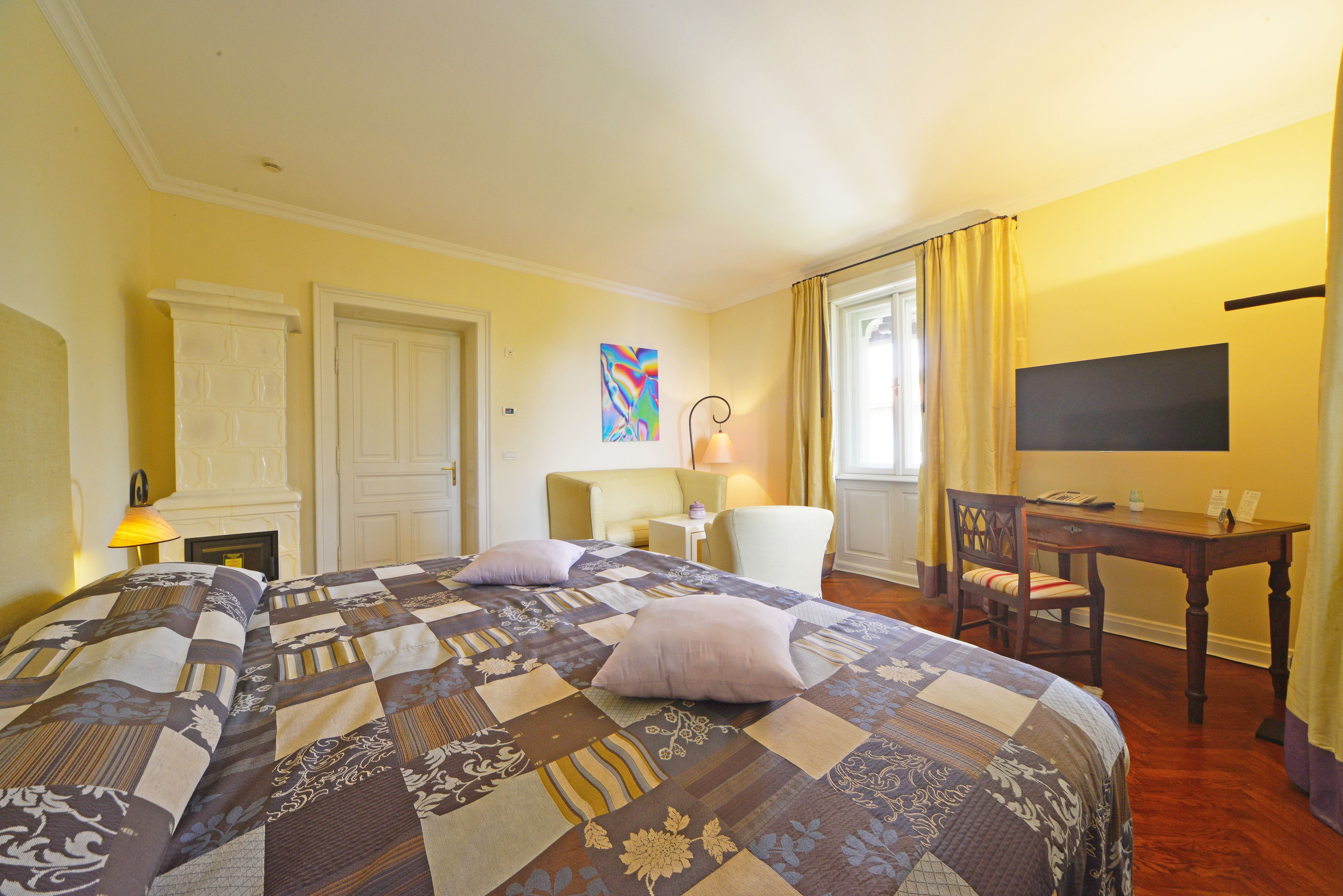 A hotel room with a large bed, a desk, a chair, a television, and a painting on the wall.