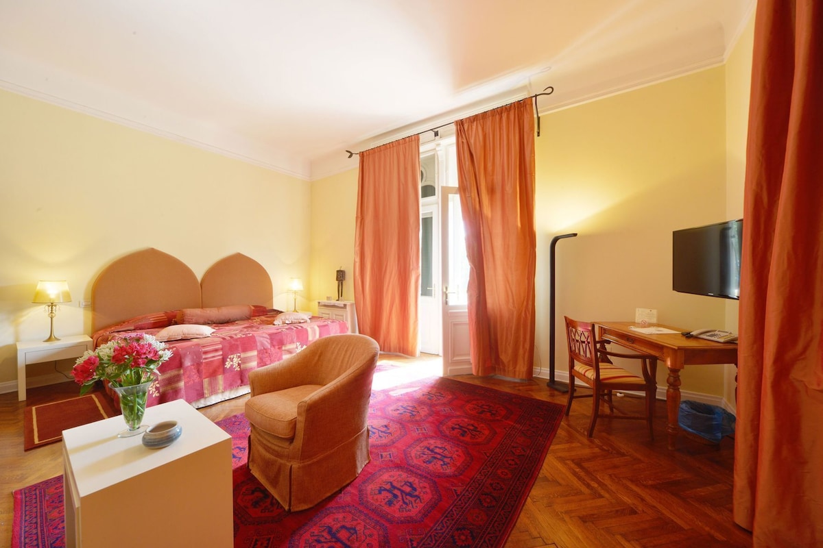 Habitación de hotel con cama, escritorio, silla, televisor y ventana con cortinas.