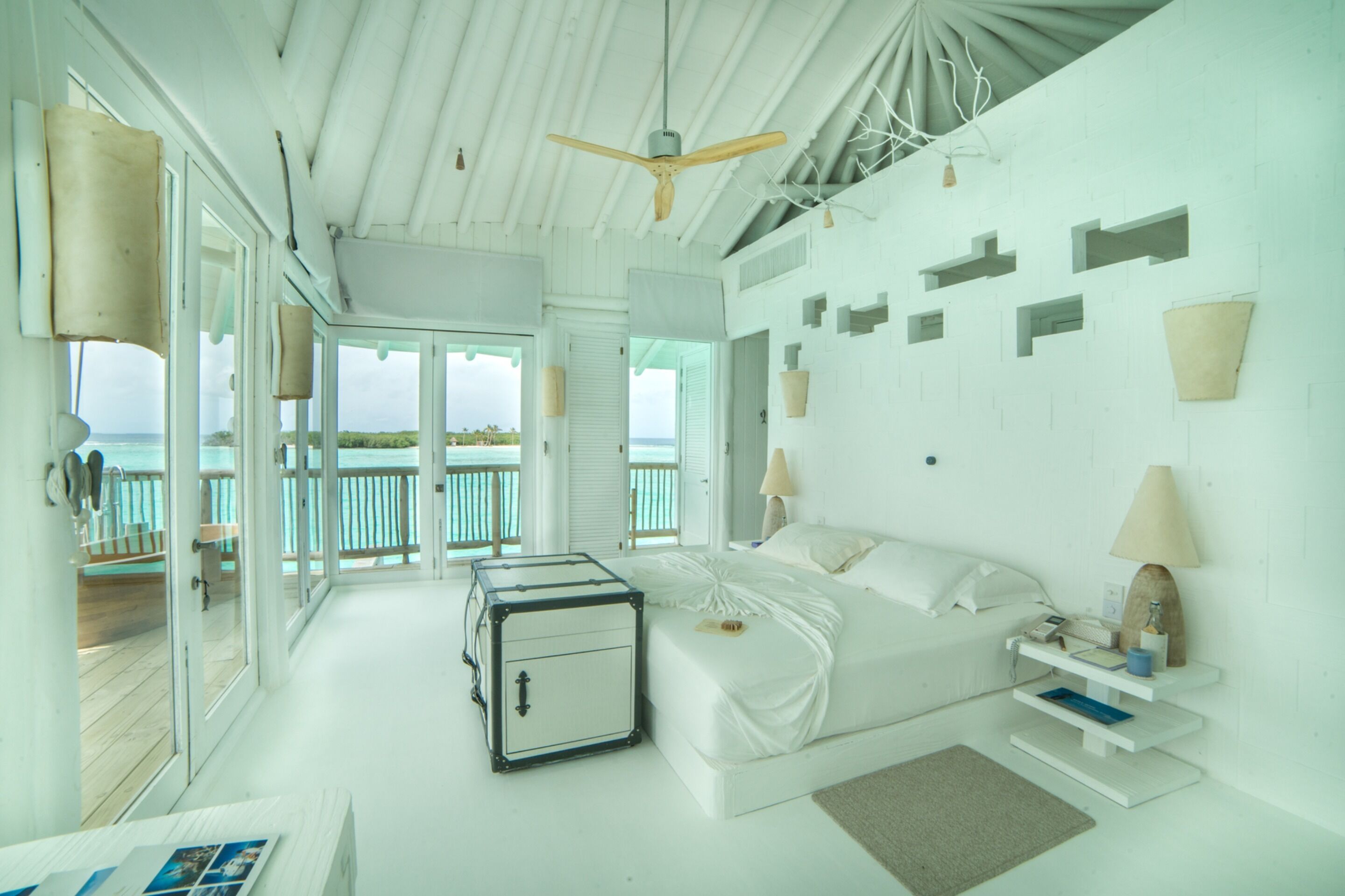 Une chambre à coucher décorée dans des tons de blanc, avec un lit, une table de chevet, une lampe et une valise.