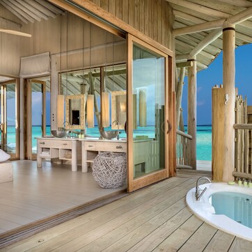 A wooden deck with a bathtub, a wooden-framed room with a large mirror, and a view of the ocean.