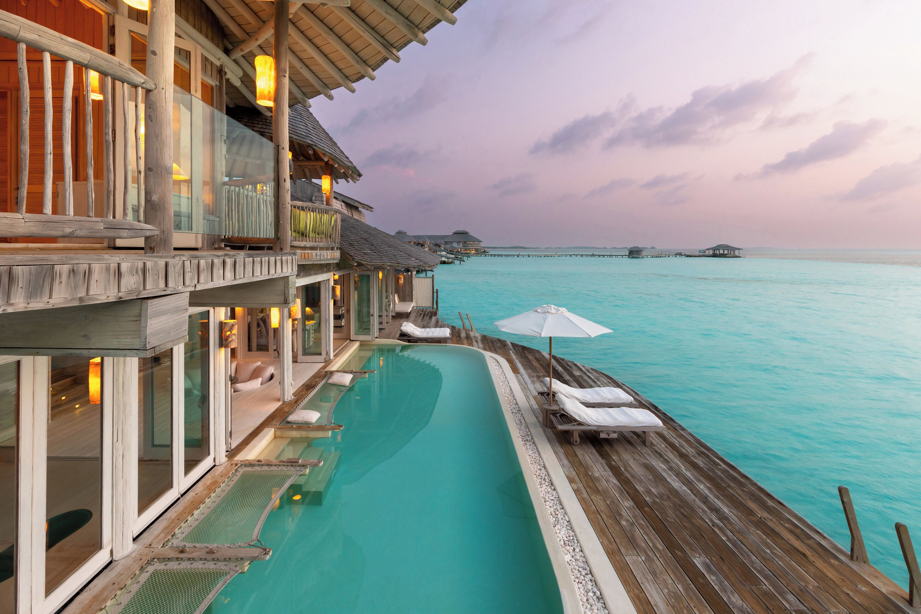 A wooden overwater bungalows with a swimming pool, lounge chairs, and umbrellas.