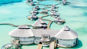 An overwater bungalows with a central building, connected by walkways, surrounded by turquoise waters. - Soneva Jani (Medhufaru)