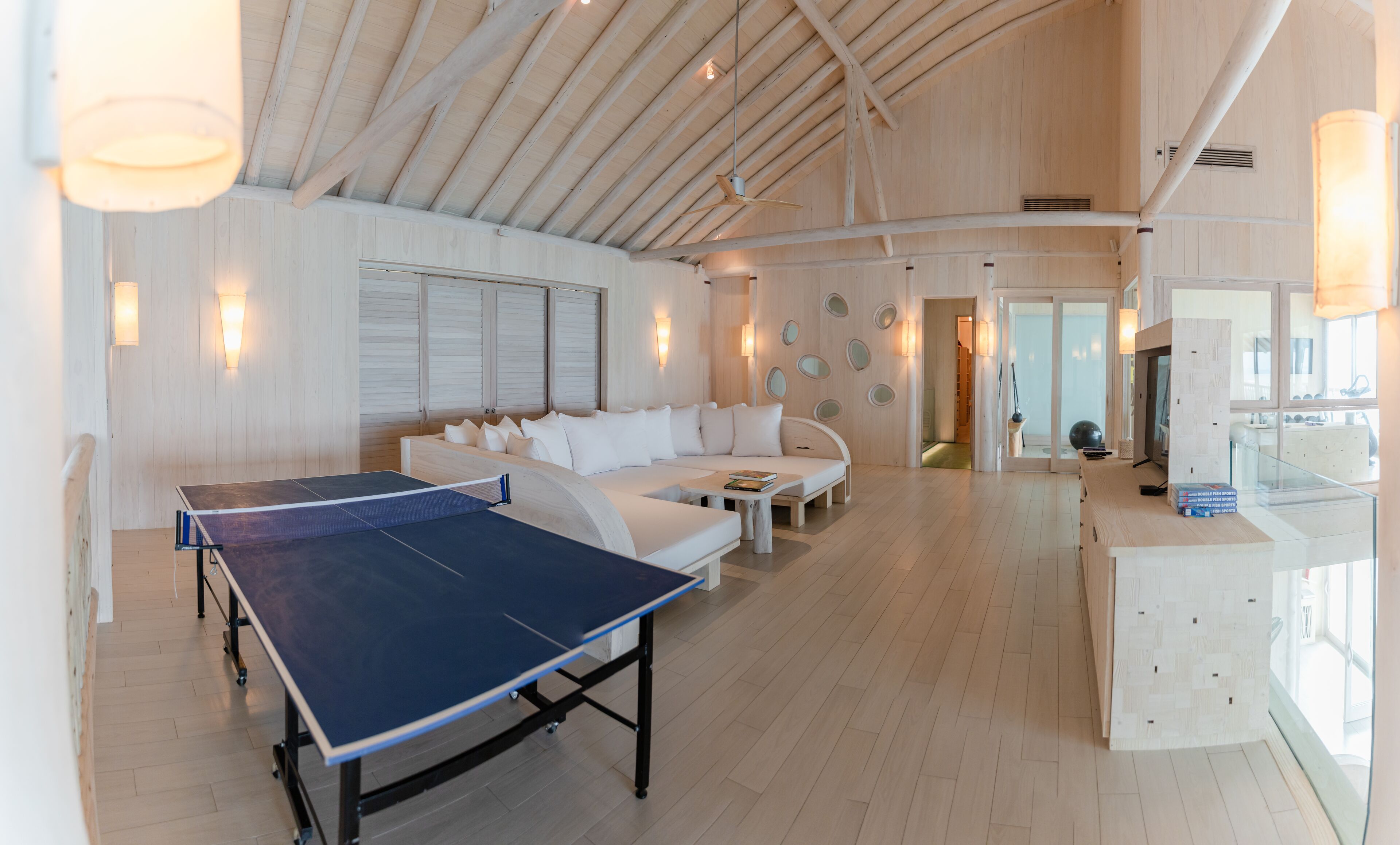 A spacious room with a ping pong table, a white sofa, and a wooden ceiling.