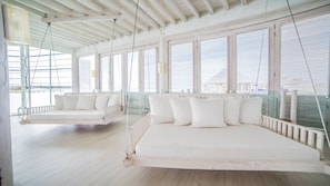A spacious room with a large bed, a swing chair, and a view through large windows.
