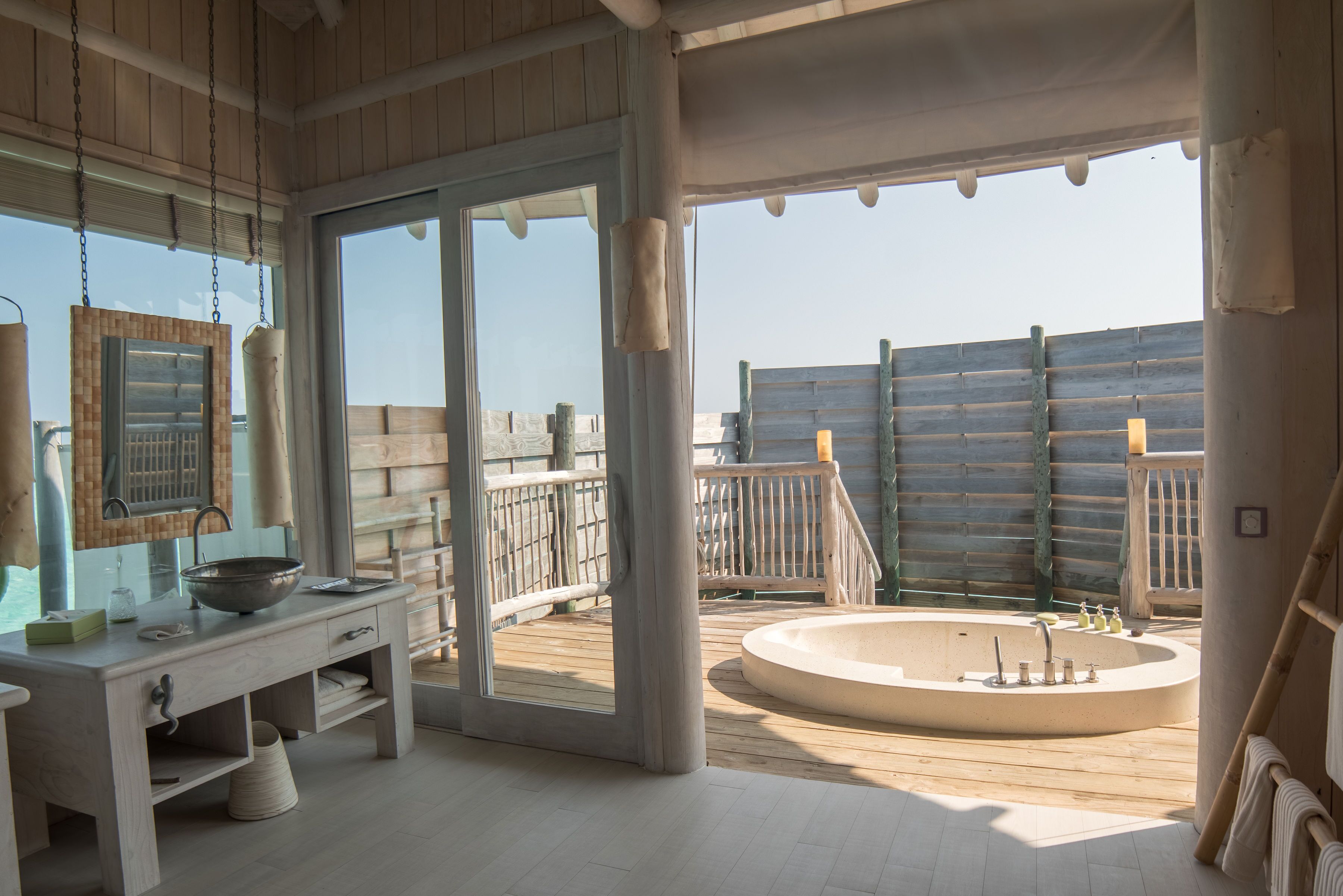 A modern bathroom with a large bathtub, a sink with a mirror, and a wooden deck outside.