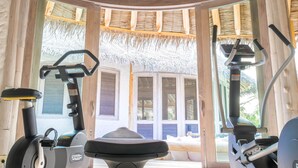A fitness room with exercise equipment, large windows, and a thatched roof.