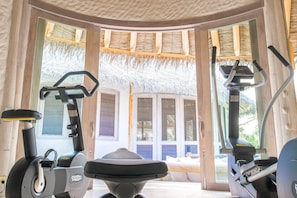 A fitness room with exercise equipment, large windows, and a thatched roof.