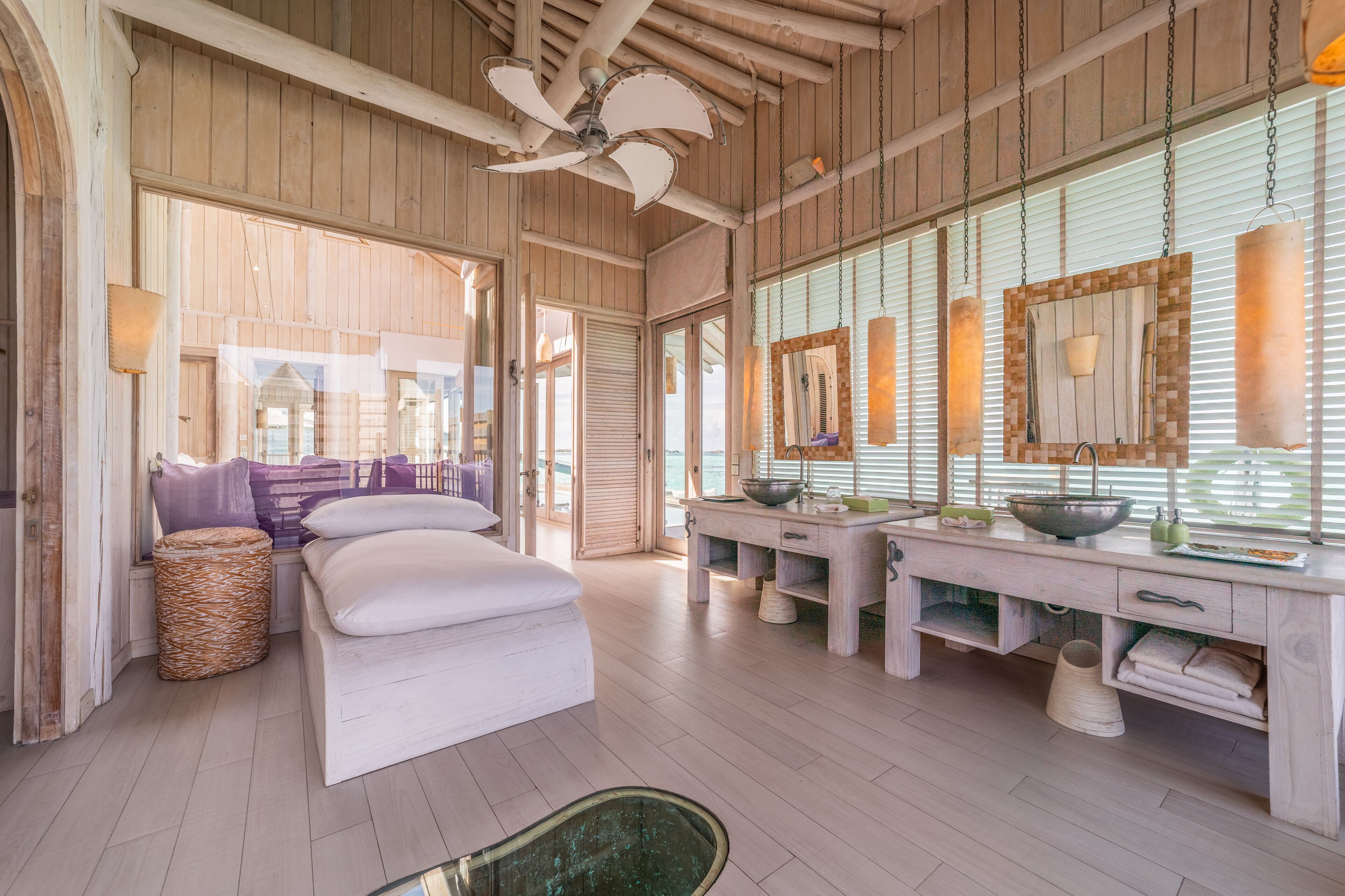 A spacious room with a wooden ceiling, a large bed, a vanity with a mirror, and a window with blinds.