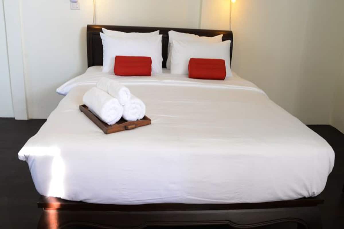 A neatly made bed with white linens and red pillows, a wooden tray with rolled towels, and a dark headboard.