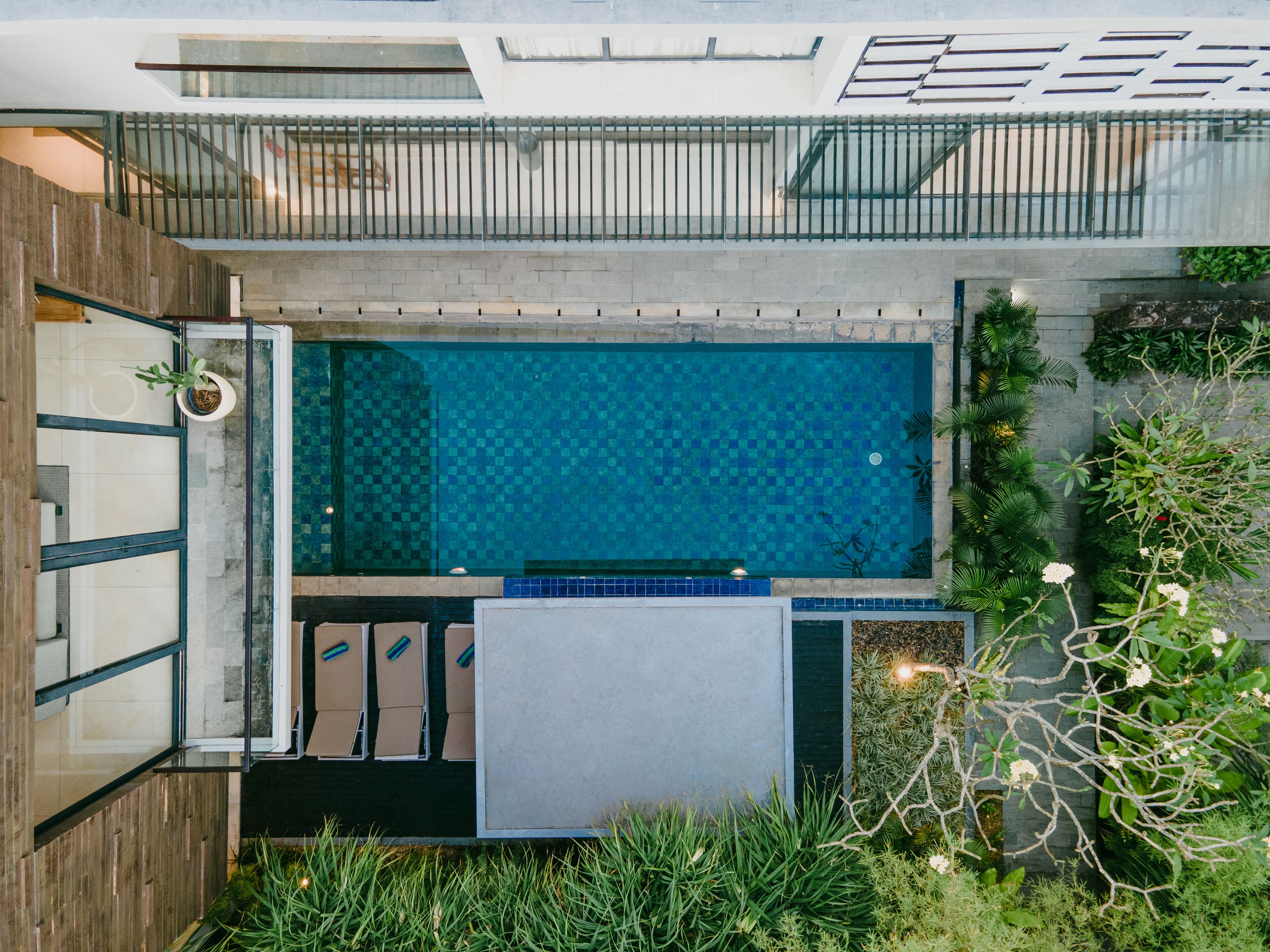 Une piscine sur le toit, dont le fond est recouvert de carreaux disposés en motif à damier, entourée de verdure et dotée d’une terrasse en bois.