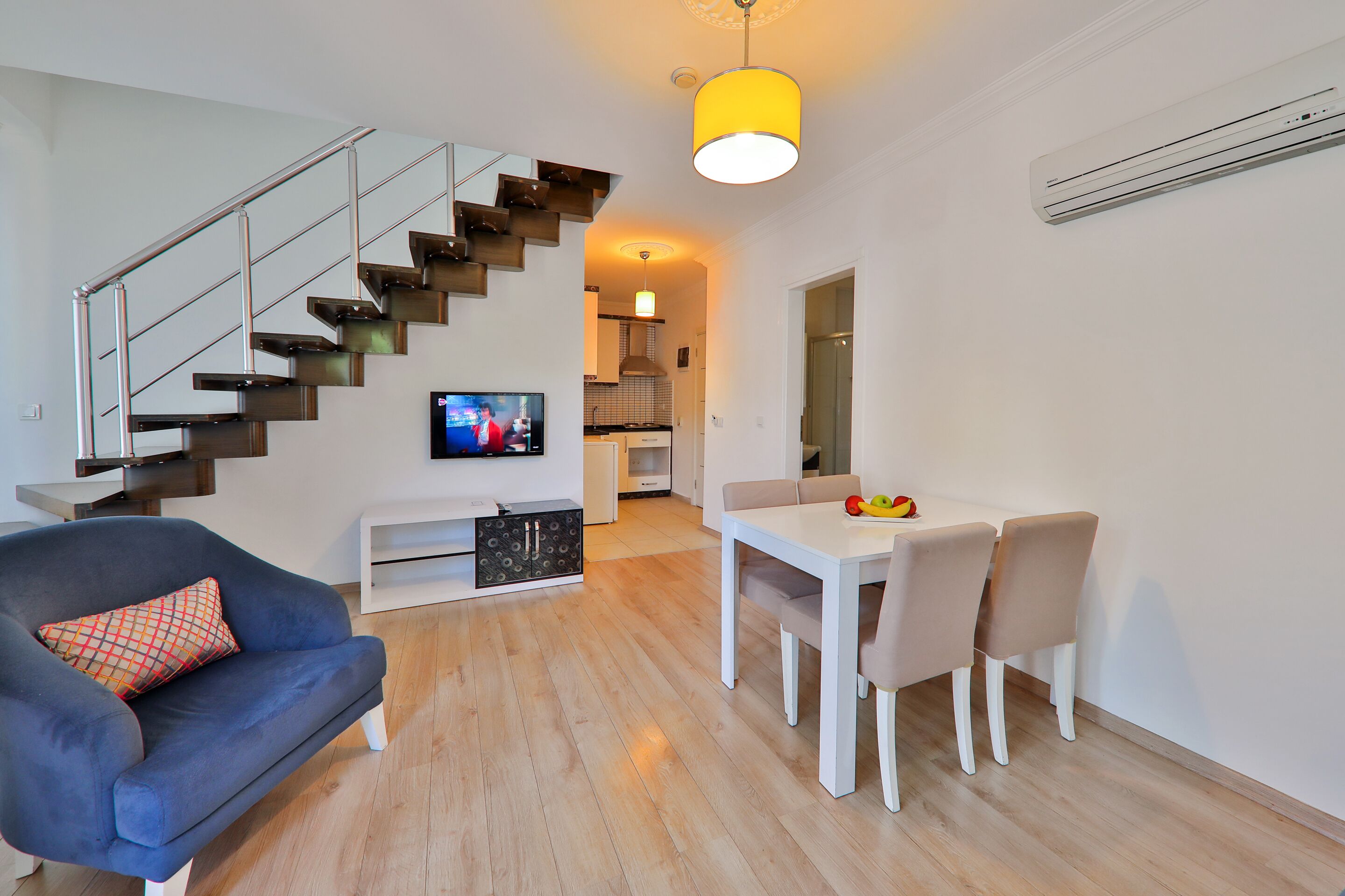 Una sala de estar moderna con una escalera, un comedor con una mesa y sillas, un sofá y un televisor.