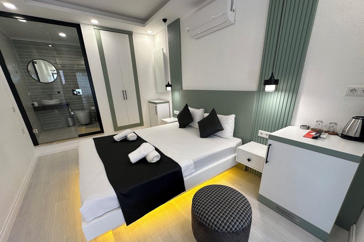 Una habitación de hotel moderna con una cama, una mesita de noche y un taburete pequeño.