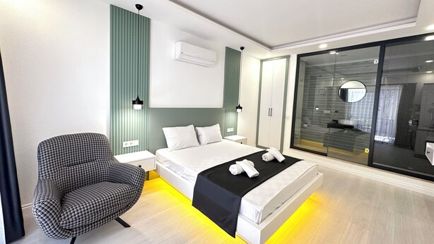A modern bedroom with a bed, bedside table, chair, and a glass-enclosed shower area. - Bossa Nova Apart (Kas)
