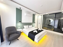 Un dormitorio moderno con cama, mesita de noche, silla y zona de ducha con paredes de vidrio.