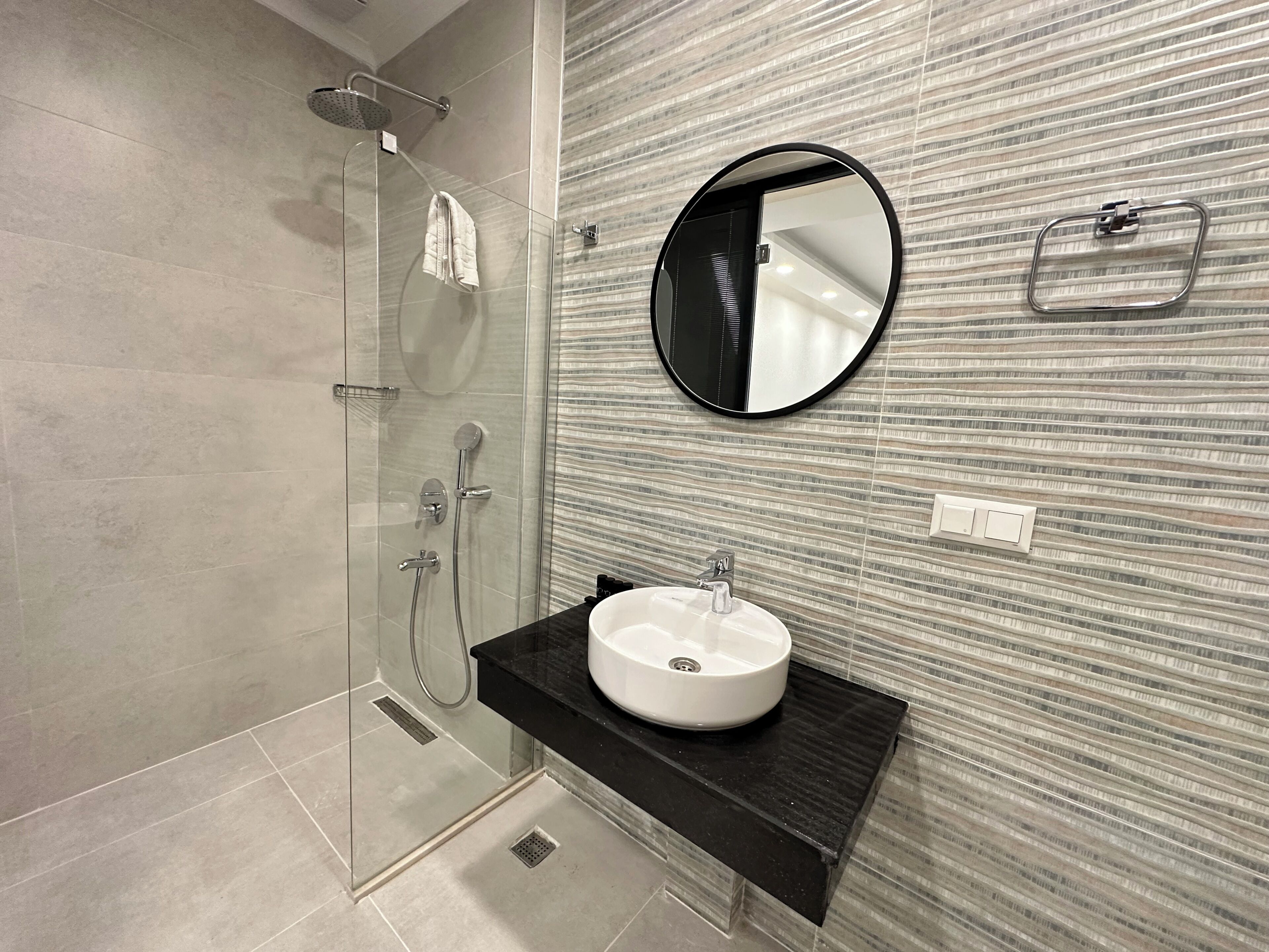 A modern bathroom with a glass-enclosed shower, a round mirror, and a black countertop with a sink.