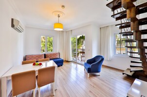 Amplia sala de estar con una mesa de comedor, sillas azules, un sofá y una escalera.