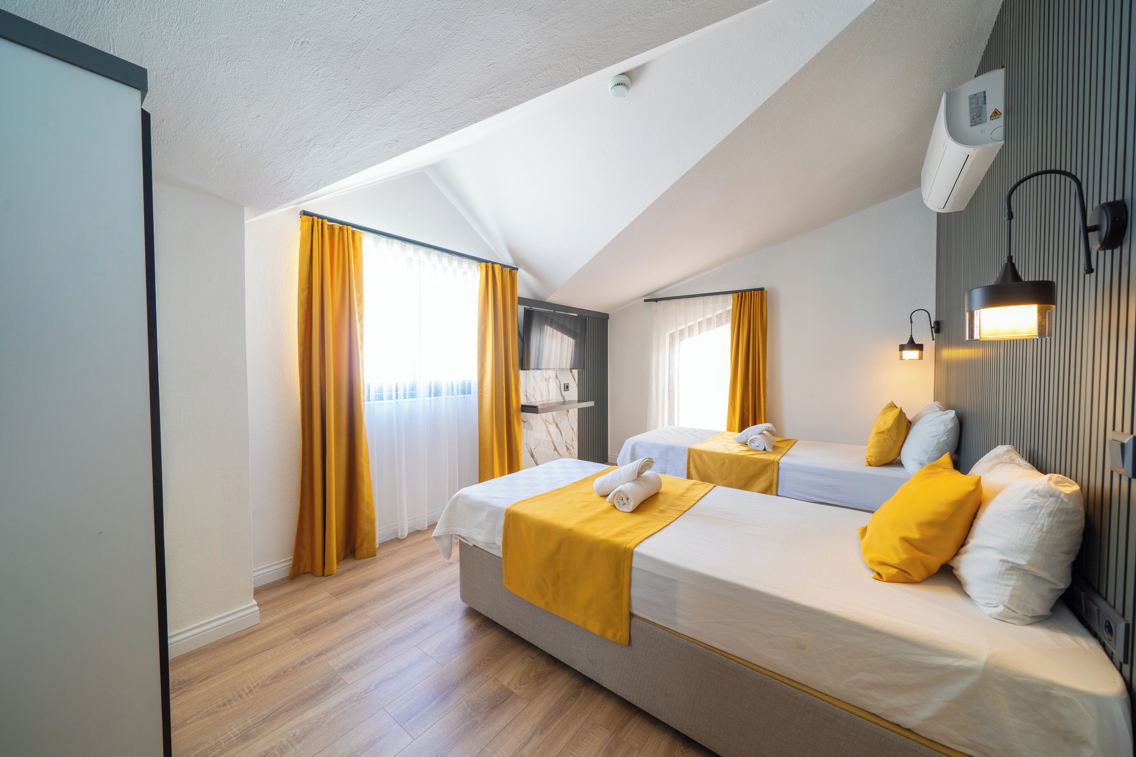 A hotel room with two beds, a ceiling fan, an air conditioning unit, and a window with curtains.