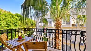 A balcony with a wooden table and chairs, a palm tree, and a view of a building with balconies. - Bossa Nova Apart (Kas)