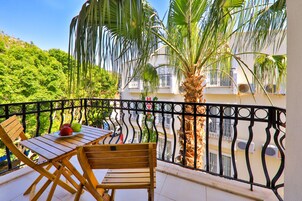 Un balcón con mesa y sillas de madera, una palmera y vista a un edificio con balcones.