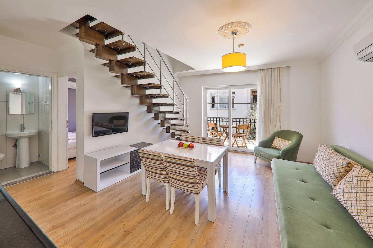 Una sala de estar moderna con una escalera, un sofá, un televisor y un comedor.
