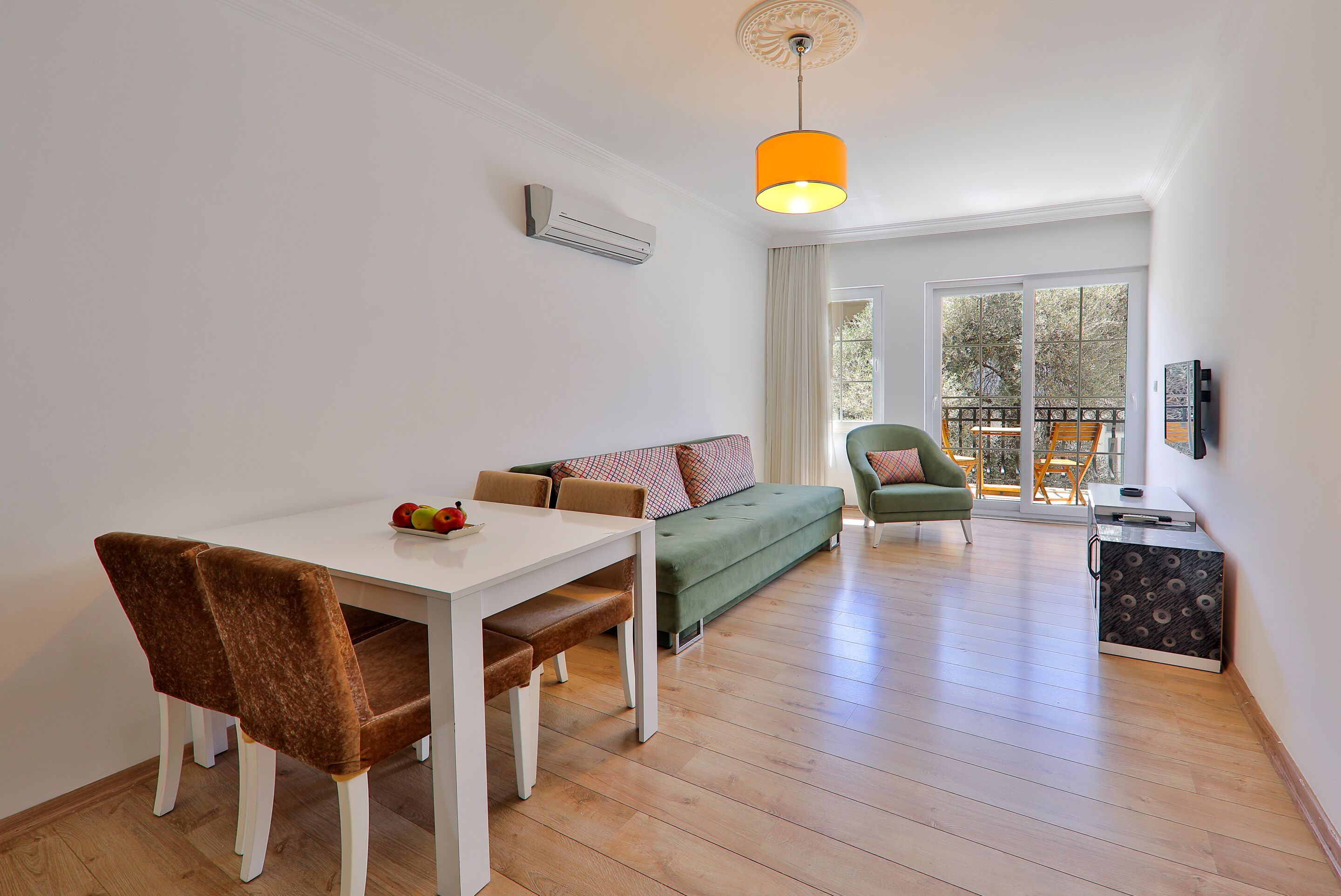 A modern living room with a white table, brown chairs, a green sofa, and a balcony with a view.