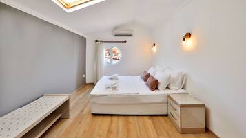 A modern bedroom with a skylight, a bed with white bedding, a bedside table, and a small wooden bench.
