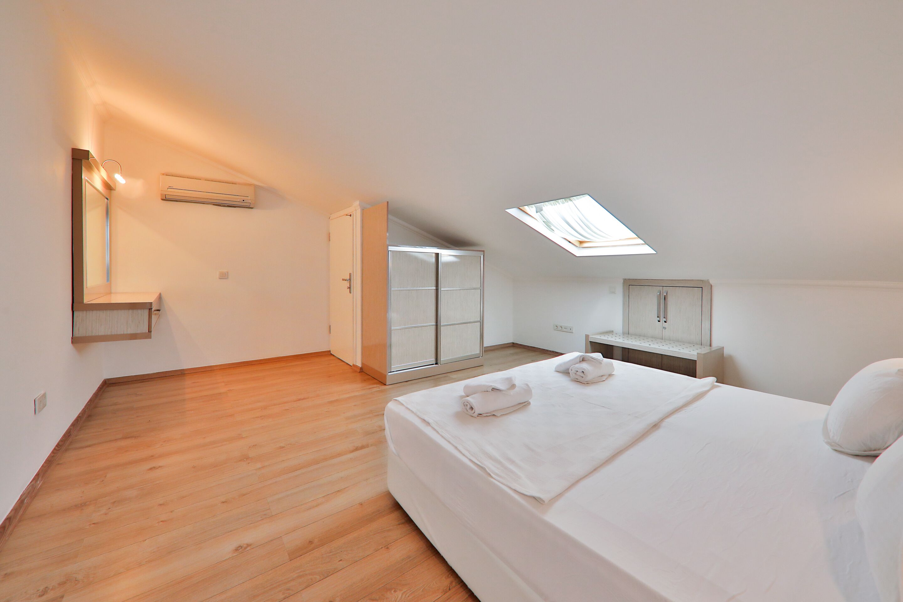 A bedroom with a skylight, a bed with towels, a wardrobe, and a bedside table.