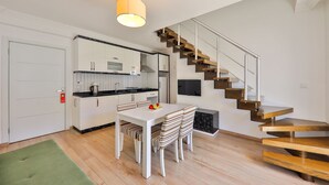 A modern kitchen with white cabinets, a black countertop, and a dining area with a white table and striped chairs. - Bossa Nova Apart (Kas)