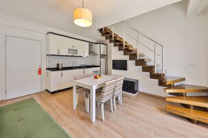 Una cocina moderna con armarios blancos, una encimera negra y una zona de comedor con mesa blanca y sillas a rayas.