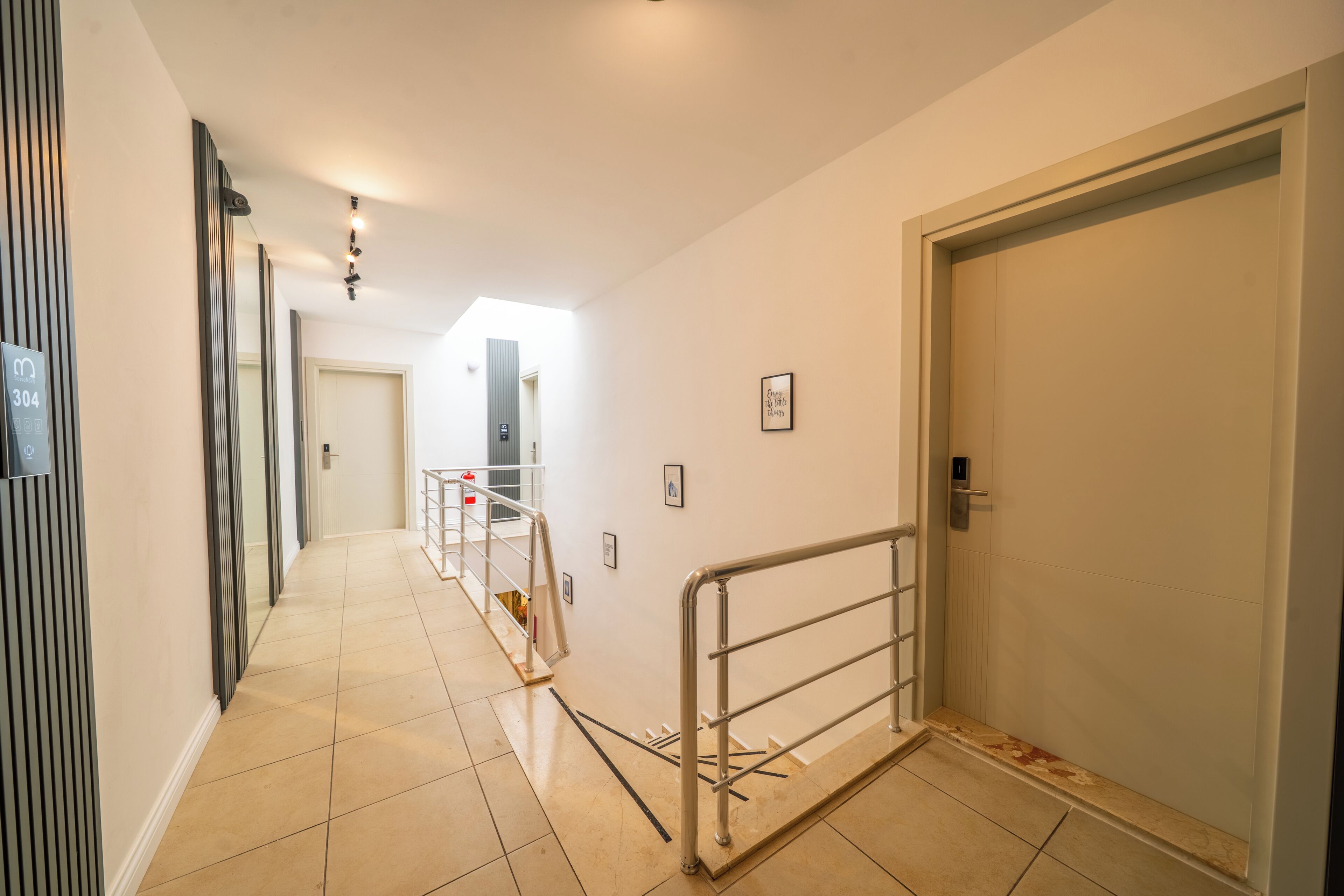 A corridor with a metal railing, a door, and a staircase leading to another level.