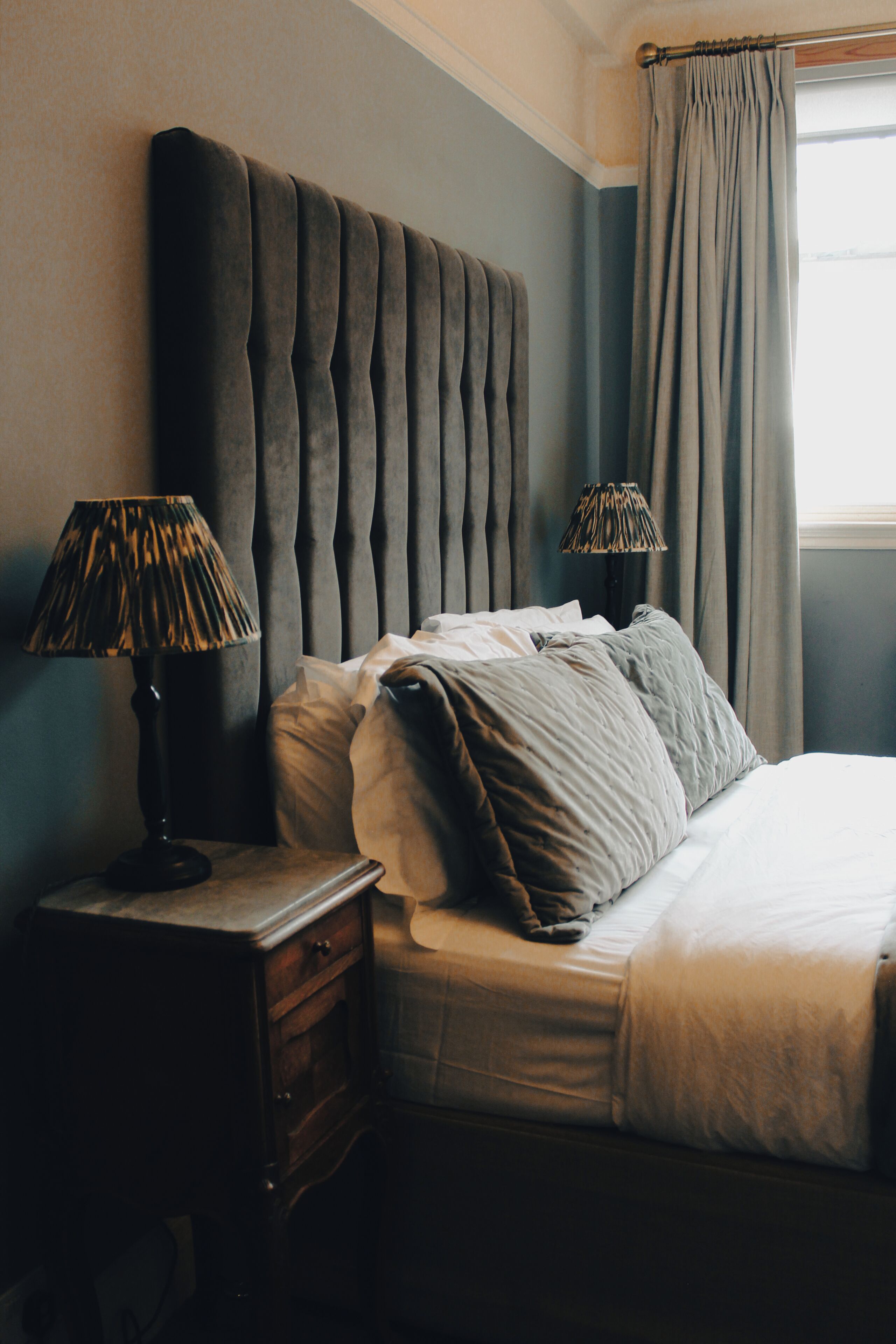A bedroom with a tufted headboard, a bedside table with lamps, and a bed with pillows.