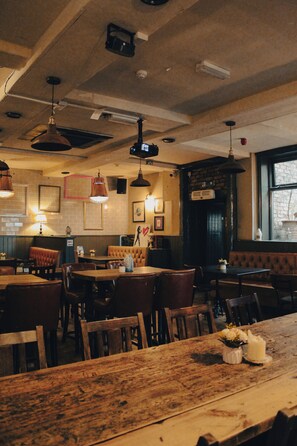 A restaurant interior with wooden tables, chairs, hanging pendant lights, and brick walls. - Prince of Wales - Townhouse (London)