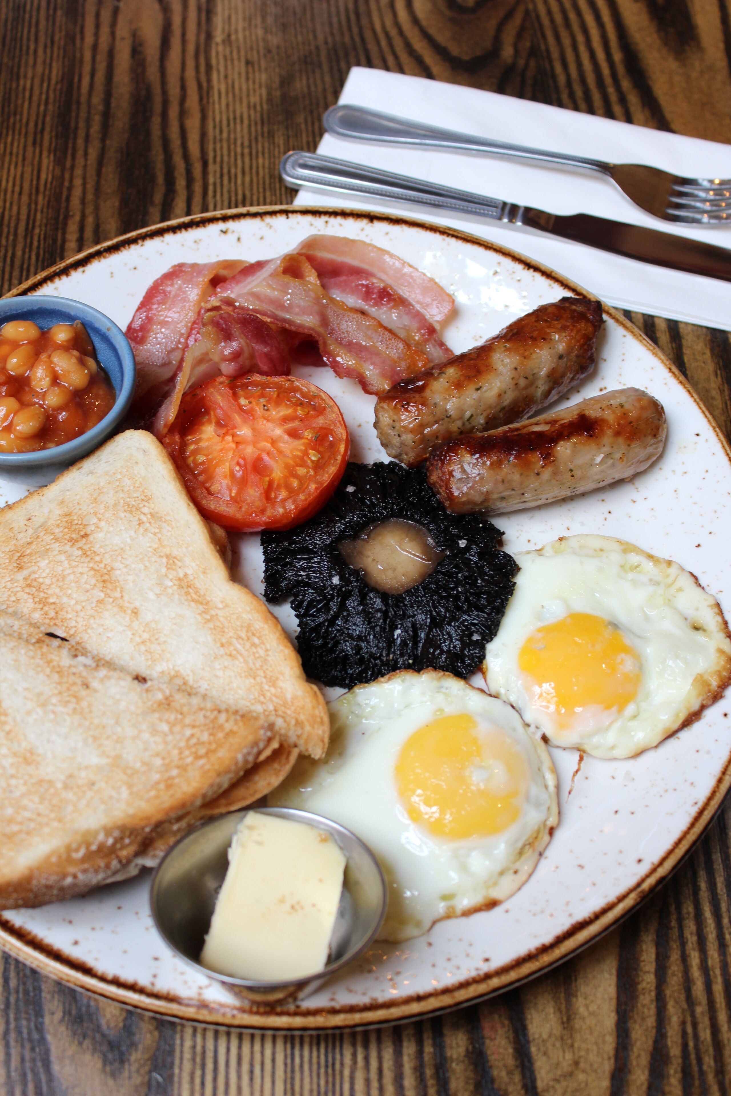 A plate of breakfast food including toast, eggs, sausages, bacon, tomatoes, and beans.