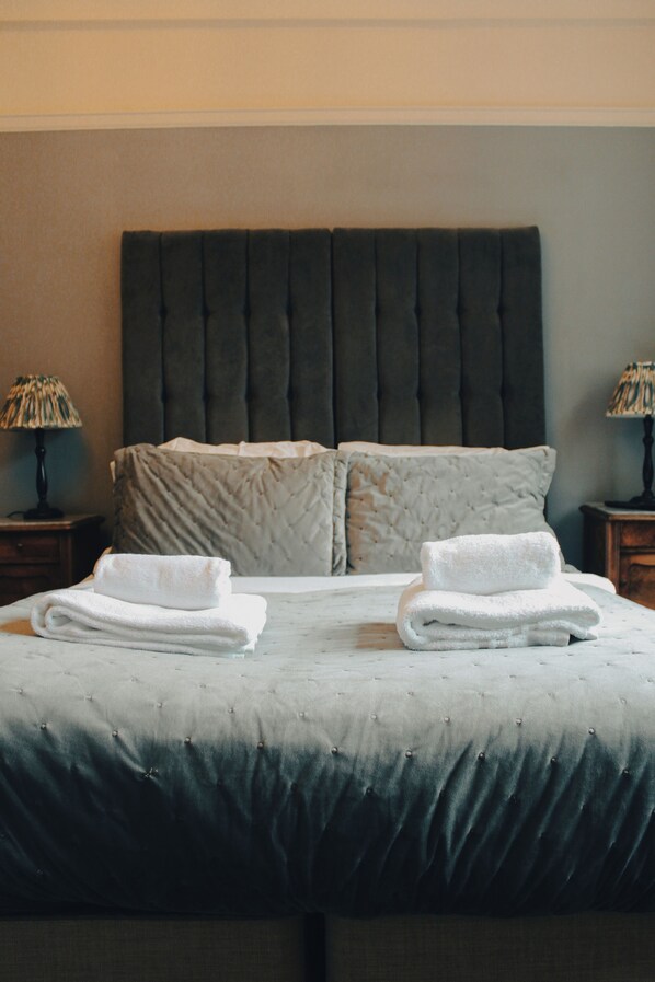 A neatly made bed with a tufted headboard, two pillows, and folded towels. - Prince of Wales - Townhouse (London)