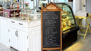 Een koffiehuis met een krijtbordmenu, witte kasten en een balkon met hekwerk.